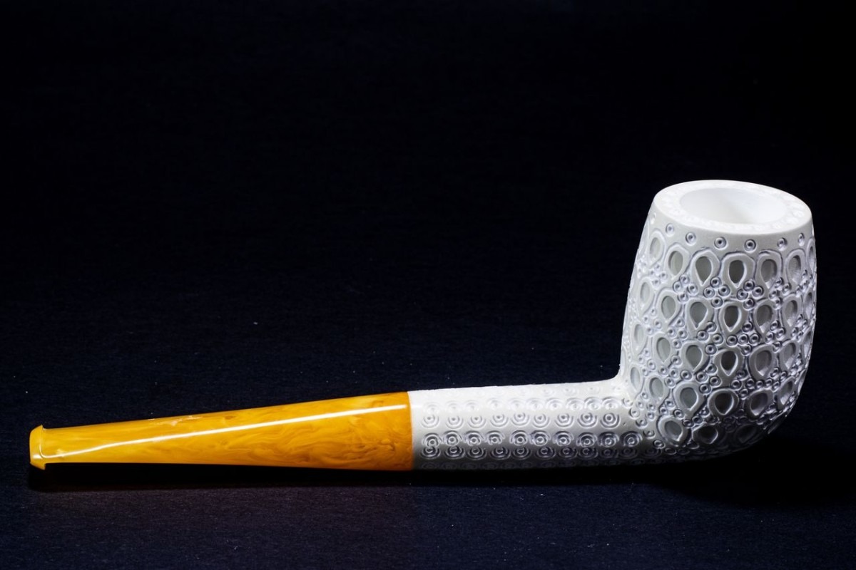 Ornately carved Meerschaum billiard pipe with a white bowl and amber-colored stem on a black background.